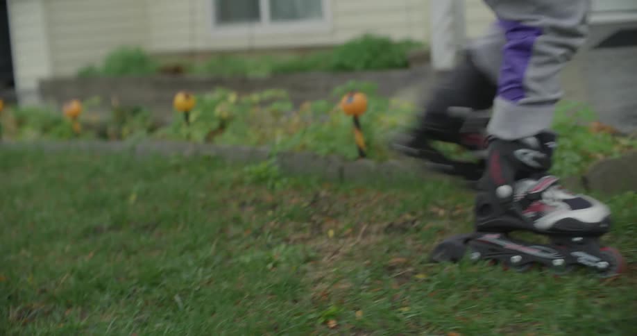 Person wearing inline skates walks across lawn near flowerbed