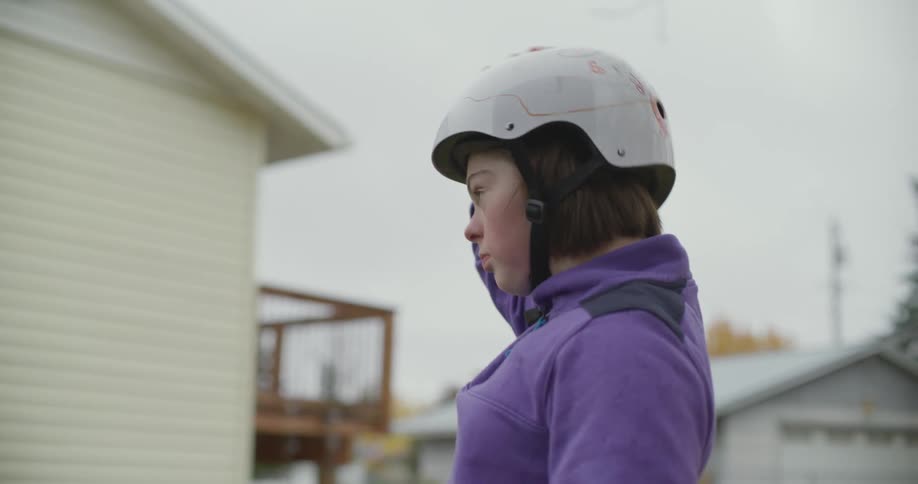 Woman helps daughter put on crash helmet while standing near house
