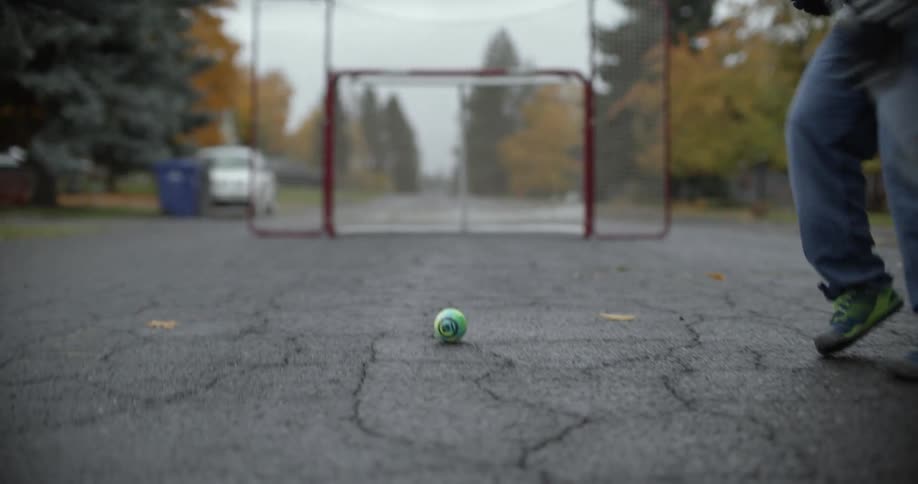 A teenage girl is using a hockey stick to shoot a ball into a goal on a gloomy day
