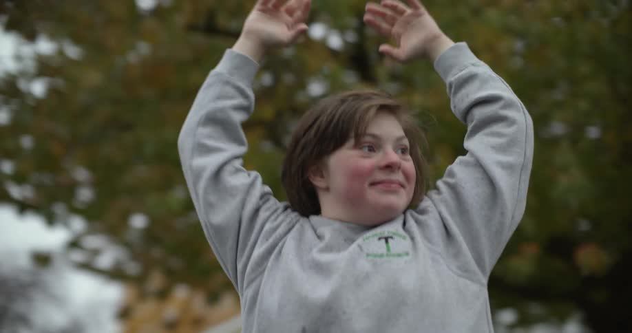 A young girl stands outside a house and raises her arms in the air as she cheers