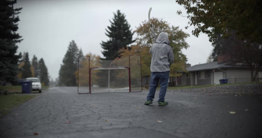 A child playing street hockey in a neighborhood street shoots a ball in to the net