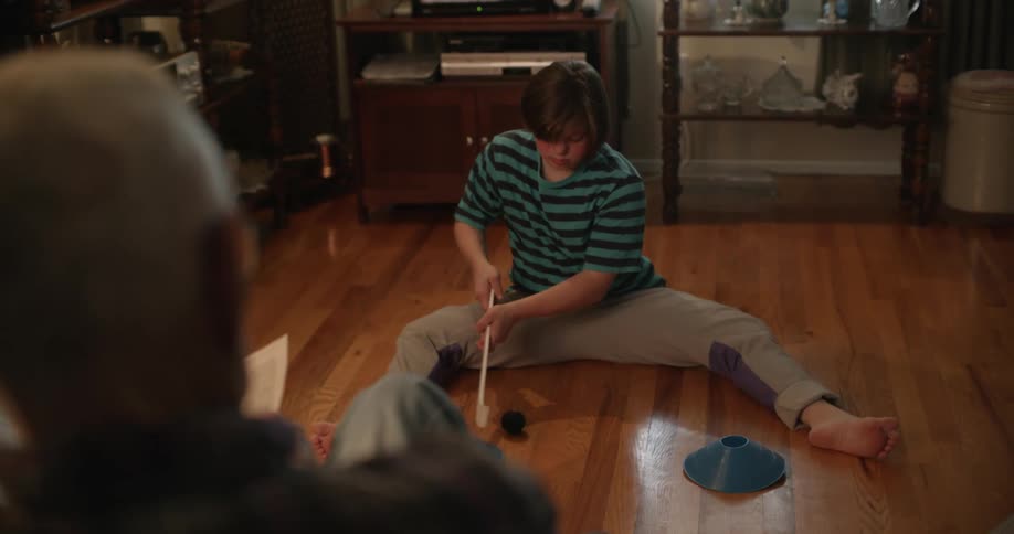 A man is reading a newspaper while a girl sits on the floor playing with toys