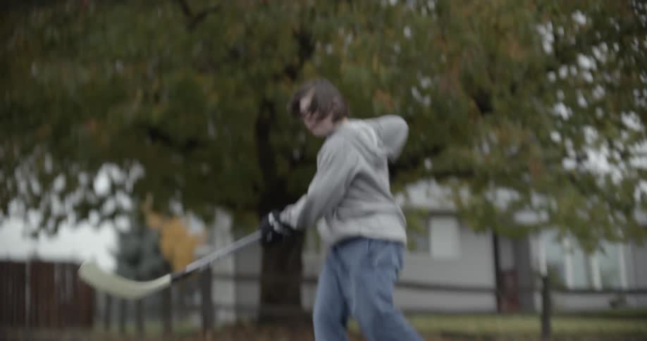 A person slacks a hockey puck in a suburban neighborhood road