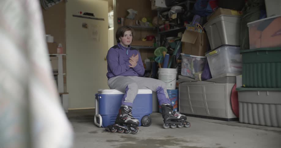 A girl sits on a cooler in her garage while wearing roller blades