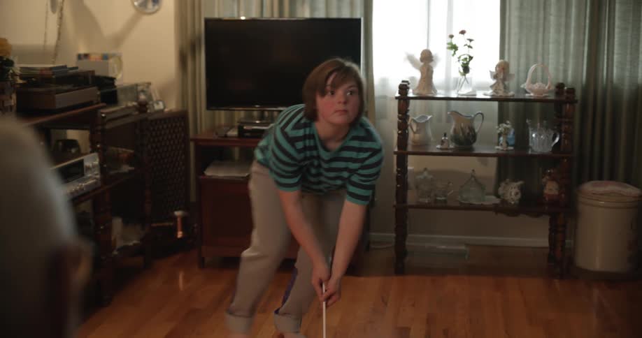 A man reads the paper as a child swings a hockey stick