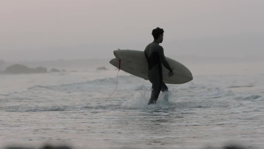 A man walks into the ocean with a surfboard