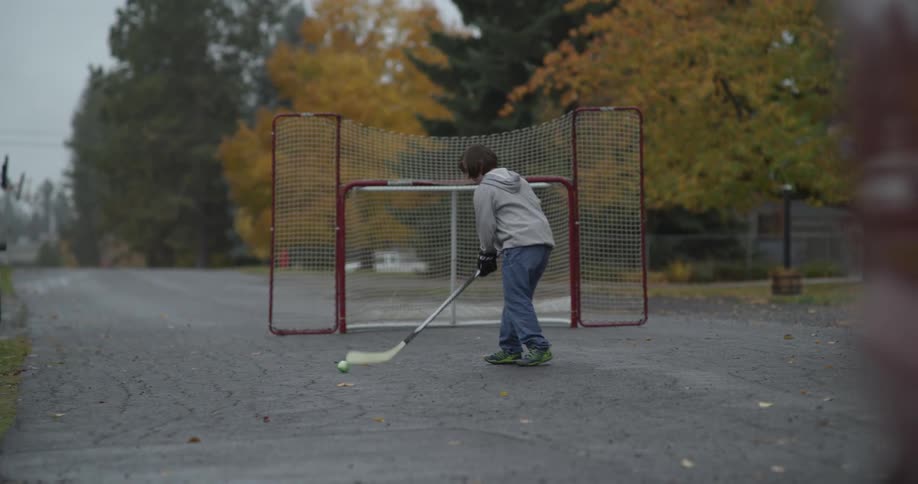 A young teenager is playing hockey and practicing goals on a neighborhood street
