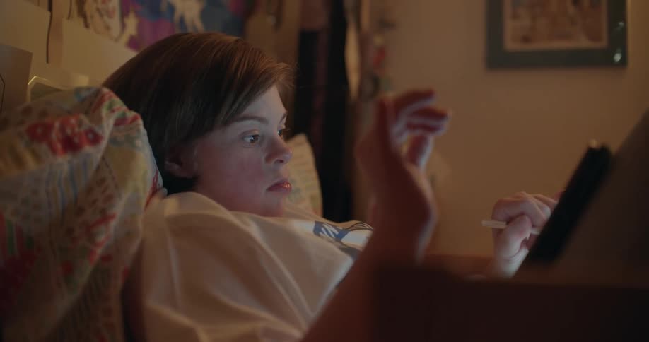 Girl with white t-shirt lying down on bed uses tablet in room