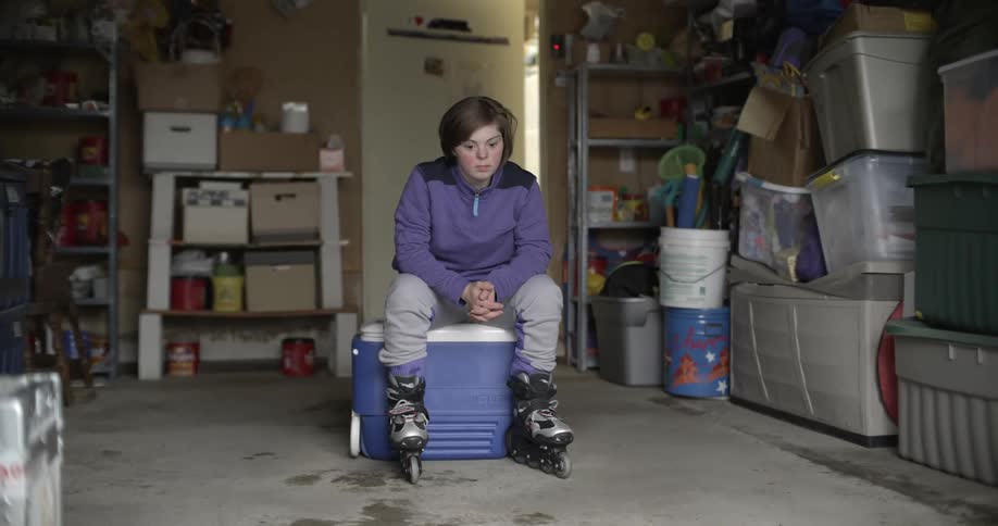 A peson sits on an ice cooler wearing roller skates in a garage