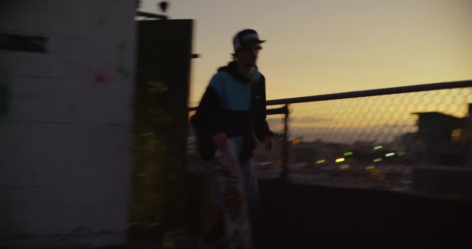 A man runs on the roof and gets on his skateboard