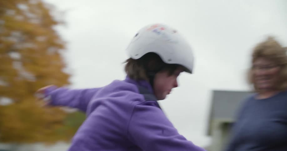 A woman smiles as she watches her mentally disabled child roller blade in front of their house