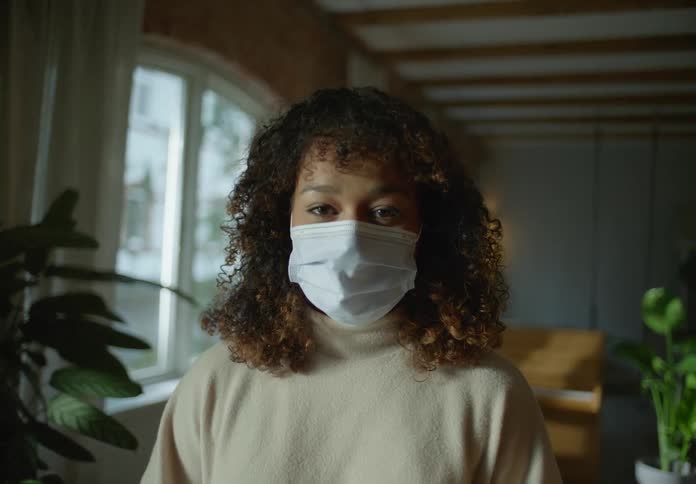 Woman stands wearing face mask in room with piano