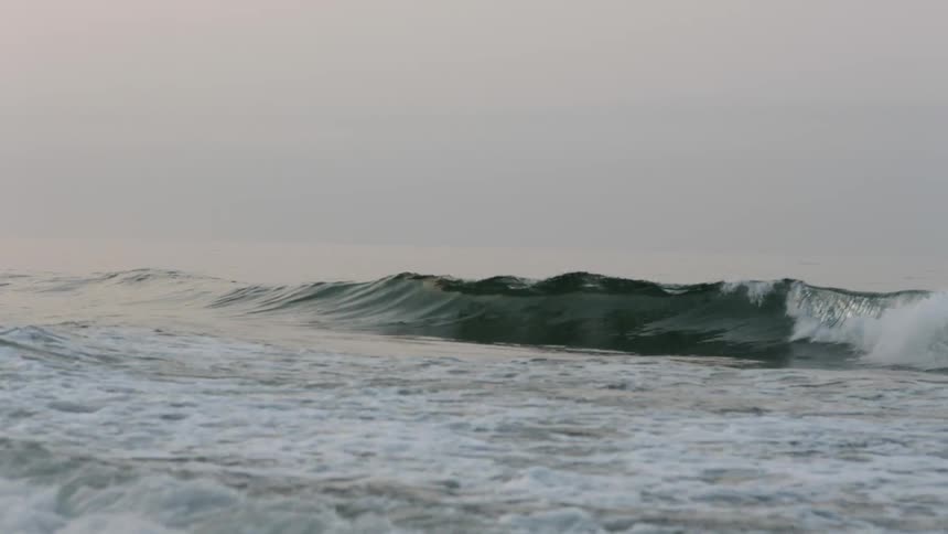 A man is surfing in some rough waves on a cloudy day
