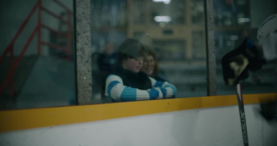 A girl leans back onto the glass after ice hockey players crash the boards