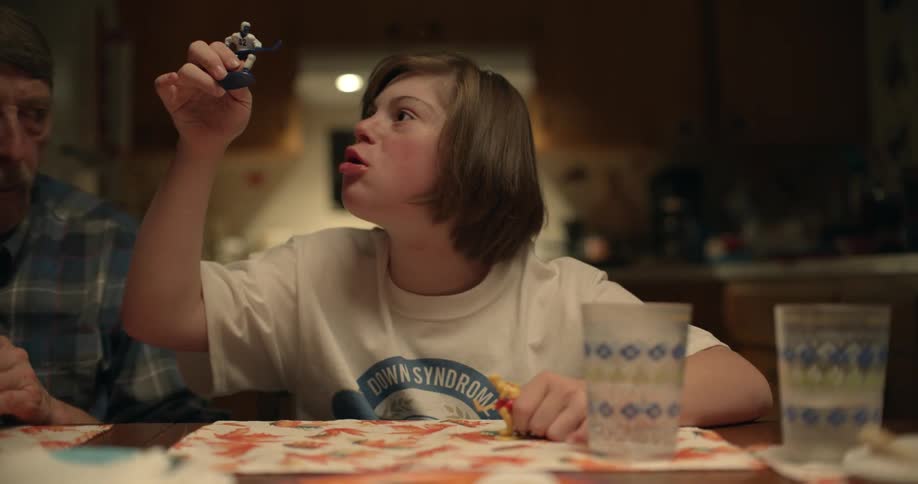 Man laughs as he watches daughter talk about figurines as they sit at dinner table