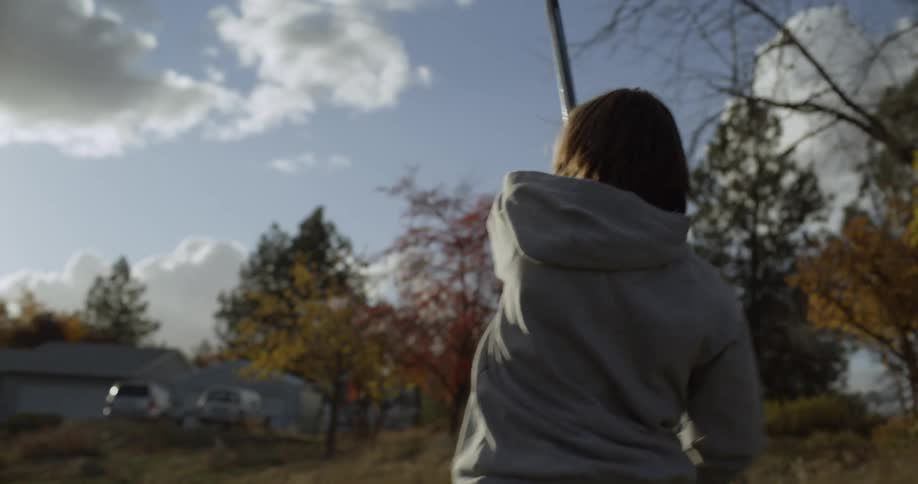 A girl is using a hockey stick to hit a ball in the yard of a home