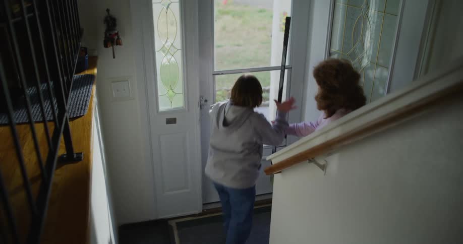 A girl runs down a hallway in a house and meets her mother at the door who has brought her a hockey stick and she grabs the stick and runs out the front door