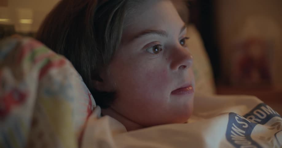 Young woman resting on a bed looking at a screen close to her face