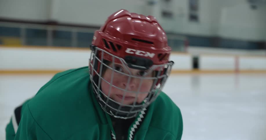 A hockey player in a hockey rink turns to look into the camera and stick out their tongue