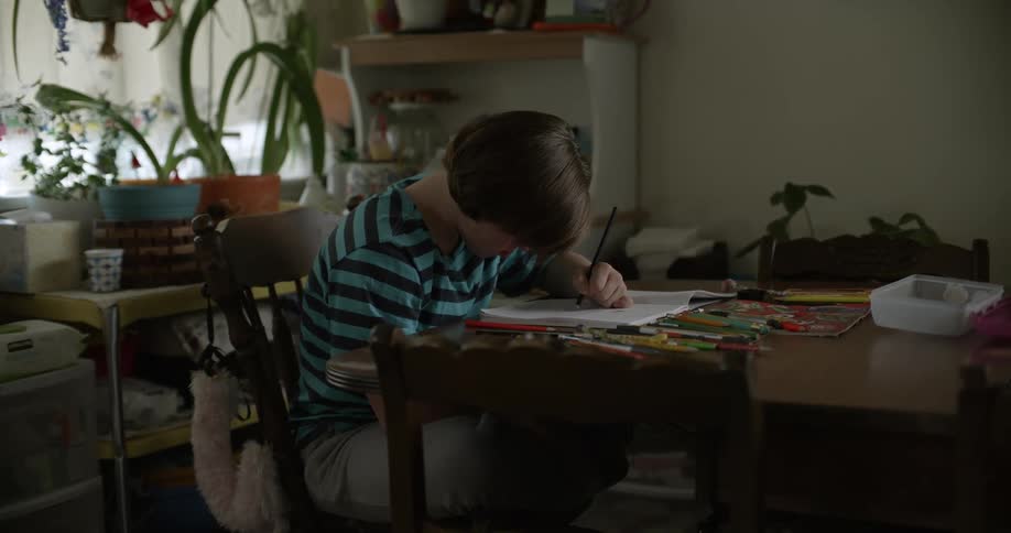 Girl with black and turquoise stripped tshirt sits at table drawing in notebook in living room at home