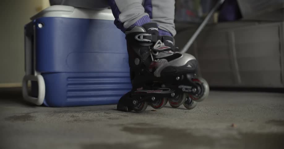 A person sits on a cooler in a garage wearing in line skates