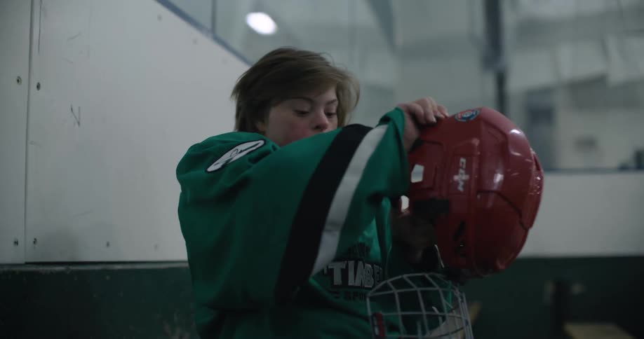 Young girl sitting on a bench in a hockey ring puts on a red helmet
