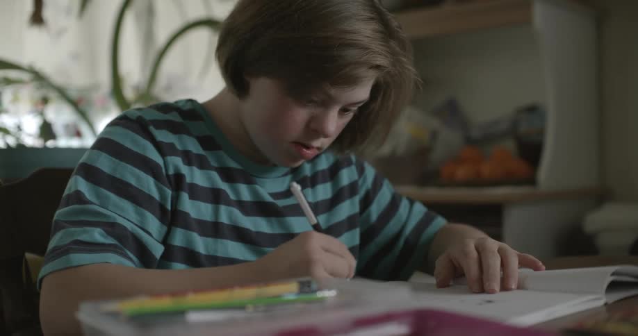 Girl with black and turquoise stripped tshirt sits at table and draws in notebook