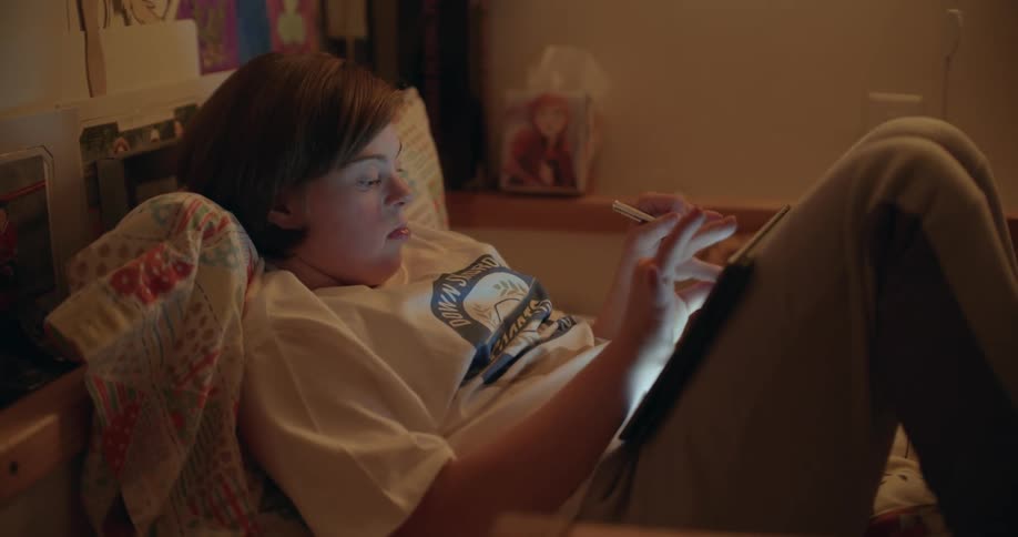 Girl with short hair white t-shirt and jeans lies on bed using tablet in her room