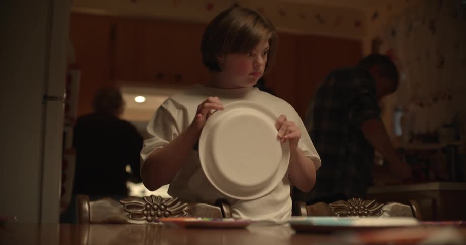 Teenage girl sets table as family works in kitchen