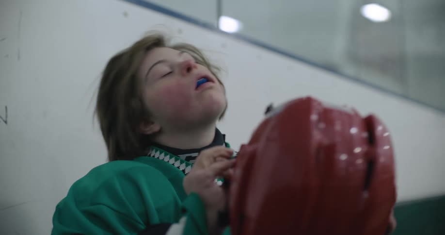 Young girl sitting on a bench in a hockey ring puts on a red helmet