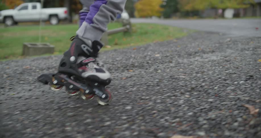 A girl struggles to use in line skates and instead walks down the road