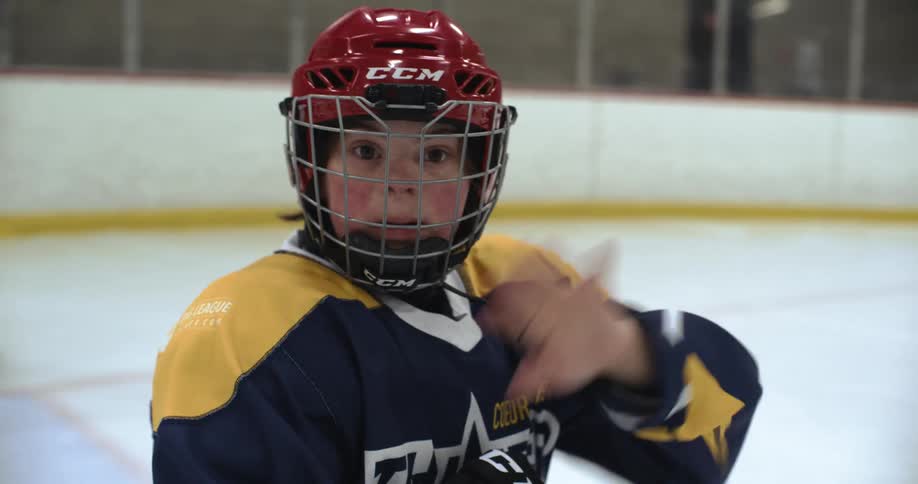 A young hockey player waves while on the ice at a rink