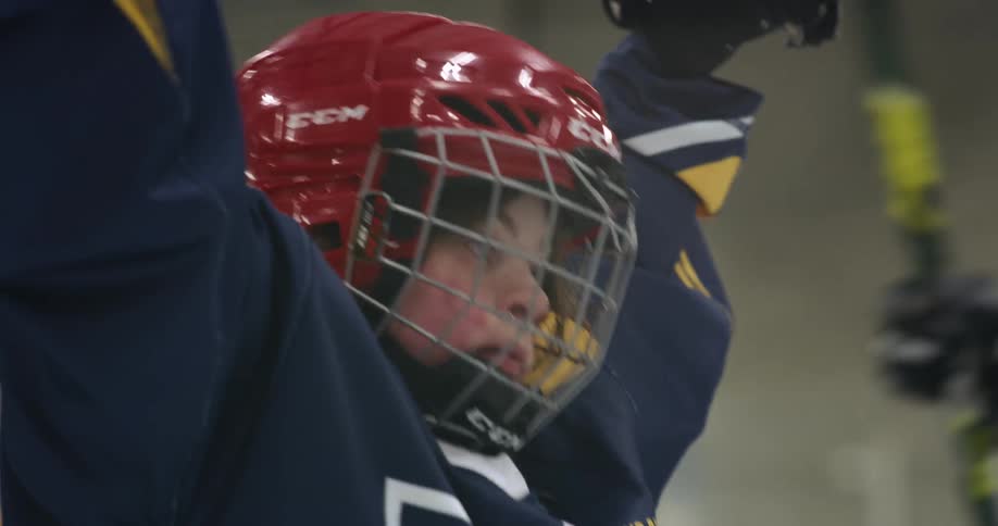 A young girl wearing hockey equipment raises her arms in the air to cheer