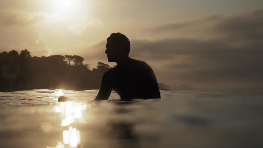 A man is floating on his surfboard at sunset