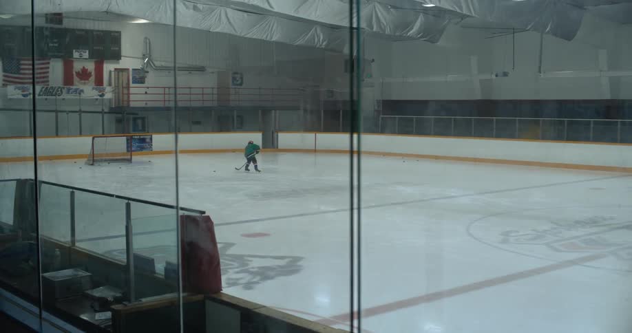 A hockey player shoots the puck on the rink alone