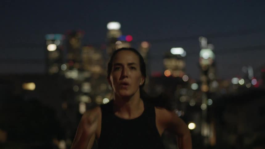 A woman is running at night with a city behind her