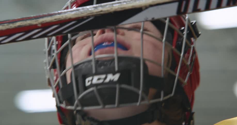 Two hockey players in protective gear smile in arena under ceiling lights