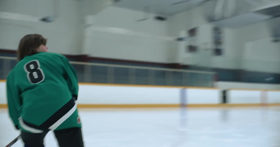 A young hockey player practices hitting pucks into the net in an ice rink