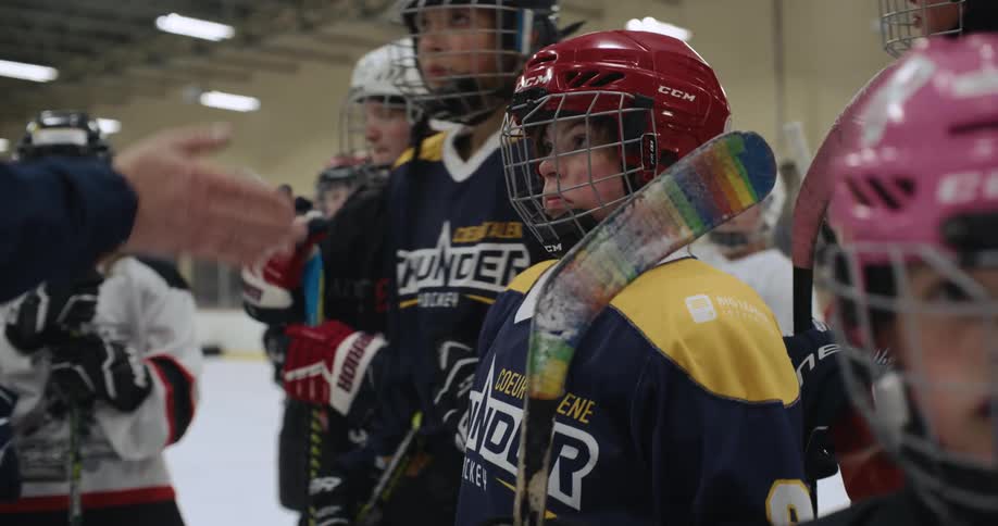 Team of young kids wearing hockey team uniforms huddle up on the skating rink