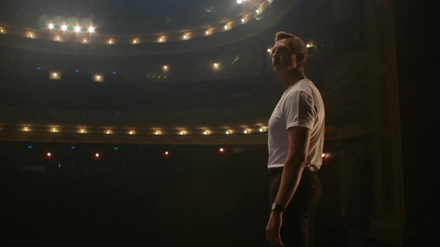 Trainer stands close to a ballet ballerina holding a dance pose over the stage on a closed theatre