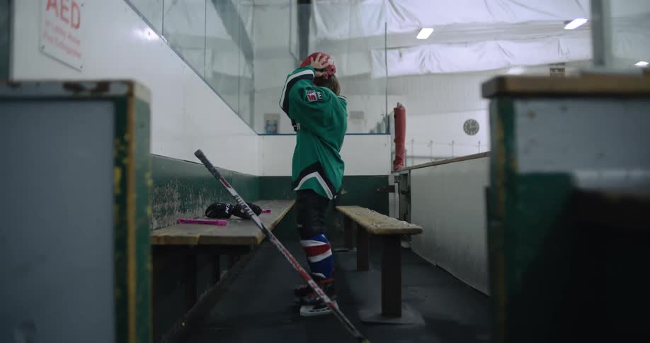 Young girl standing next to a bench in a hockey ring puts on a red helmet