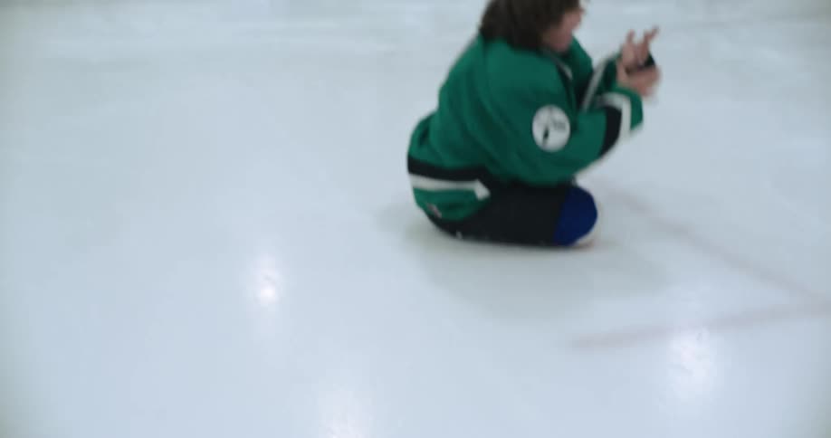 A girl in hockey gear is ice skating then falls as she comes to a stop and appears injured