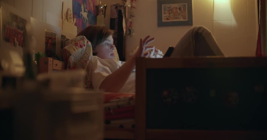 Girl with white t-shirt and jeans lies on bed using smartphone in room