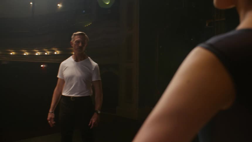 A man walks on a stage and turns to look at the woman standing waiting to begin dancing