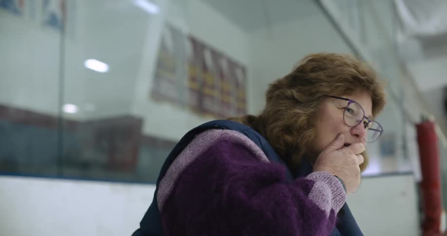 Mother watching her daughter practicing ice hockey on an ice rink