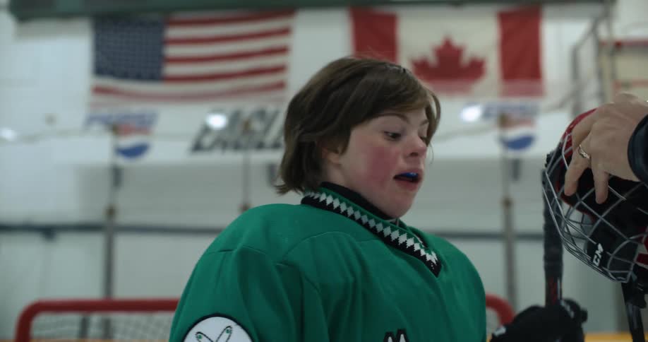 Adult helps teenage hockey player put on her mask after she teases them and put in her mouth guard