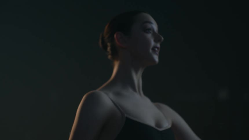 Young ballerina practices ballet poses on a stage under a spotlight