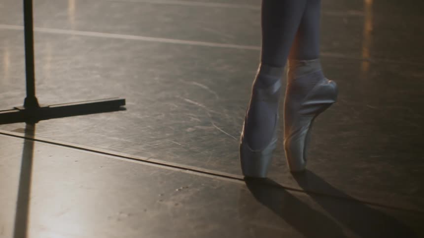 Ballerina practices en pointe next to freestanding bar