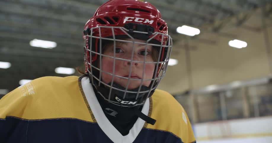 Female hockey player wearing protective gear looks around as another player skates along ice rink