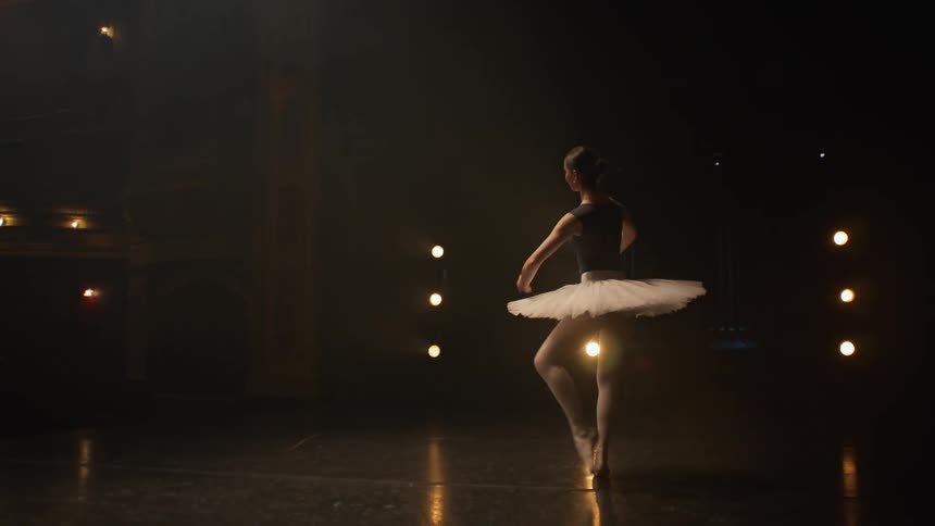 Young ballerina dancing ballet spins on an empty theatre stage